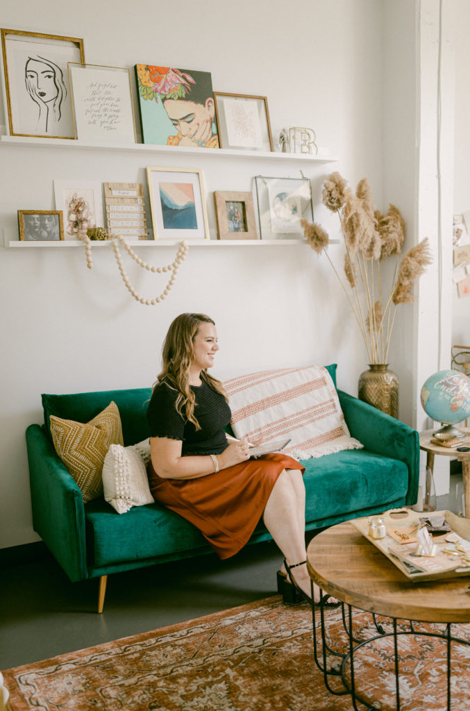 I'm Braelynn, a wedding planner and event designer. I created a workspace for my business I am in love with. You see me in this photo sitting on my emerald green sofa. Decor pieces with accents of gold and neutral for my office space.