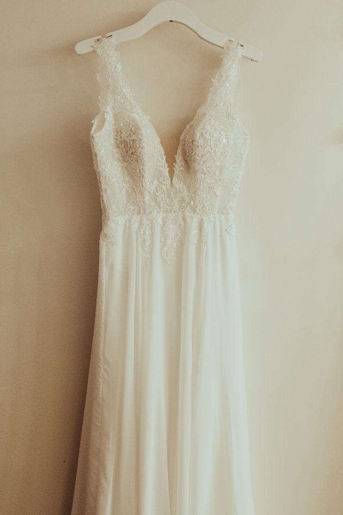 A white wedding dress with embellishments on the torso. The straps are about two inches wide and the neckline is a deep v cut.