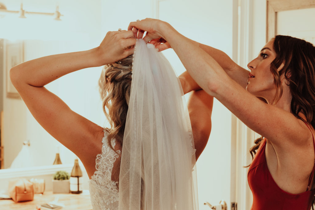 A bridesmaid helps the bride put her veil on her hair.